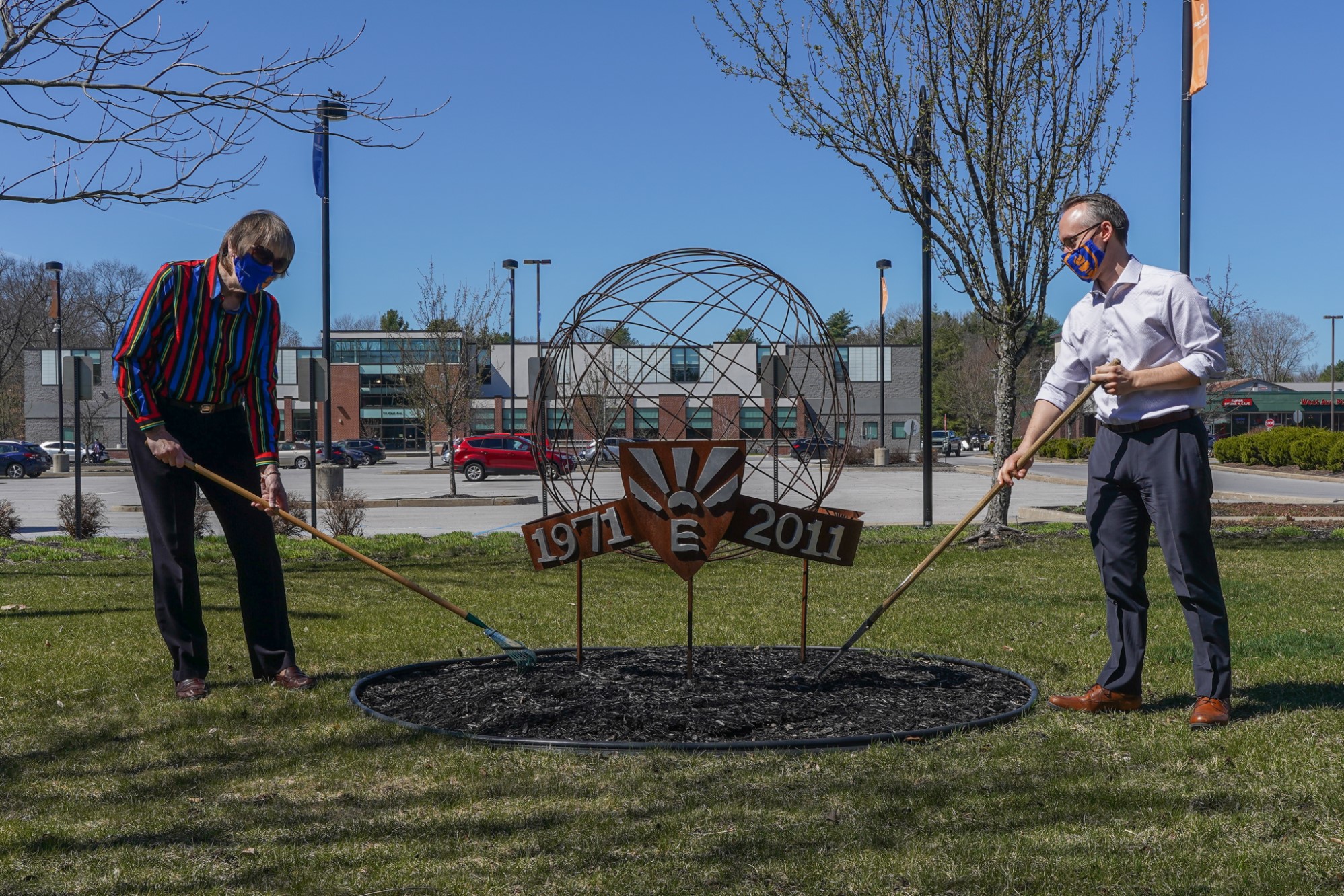 Two people planting garden in front of metal sculpture.